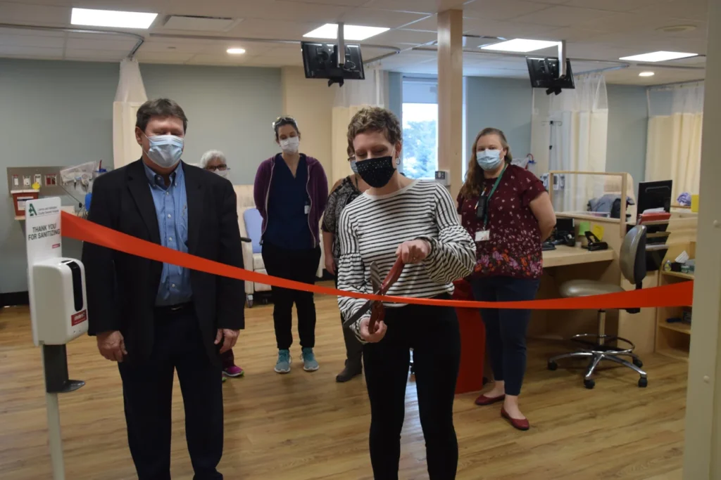 Person cutting a red ribbon indoors while others stand nearby wearing masks, marking the opening of a clinical space.