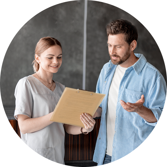 Health-care worker reviewing a document with a man, both standing and discussing paperwork.