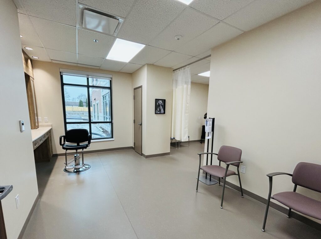 A picture of a room with a black salon style chair and two red coloured waiting room chairs spaced far apart.