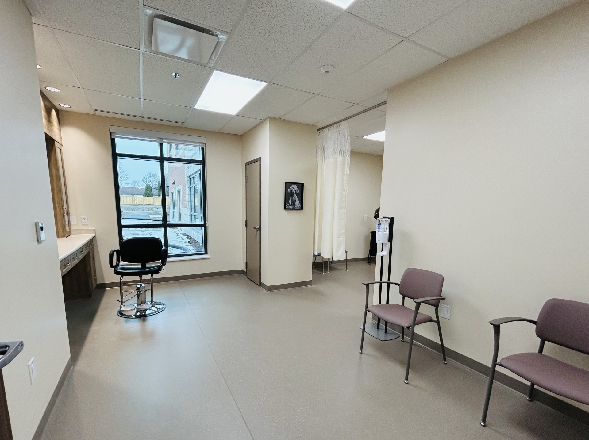 A picture of a room with a black salon style chair and two red coloured waiting room chairs spaced far apart.
